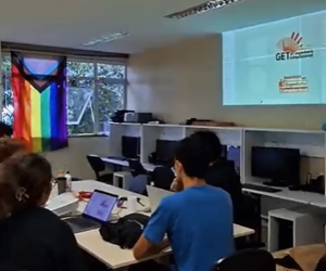 Foto pixelada com alguns membros presentes e um slide de fundo com a logo do GET Engenharia Computacional.