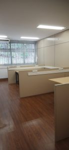 Sala com piso de laminado e mesas de escritório, com janela ao fundo