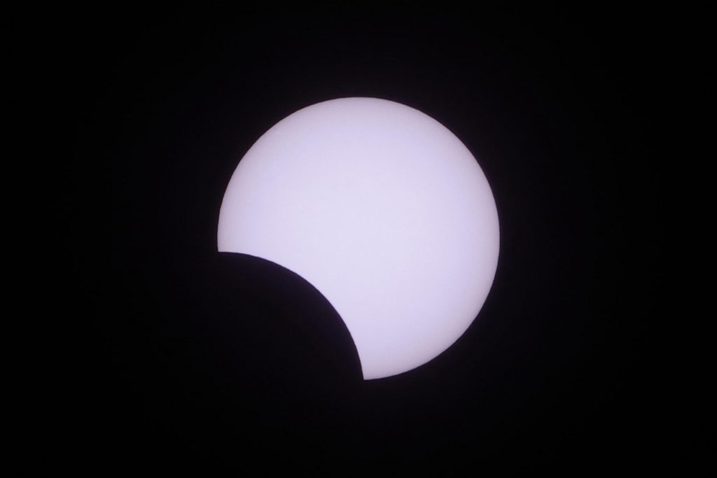 Foto do eclipse solar parcial, com a Lua tampando uma pequena parte do Sol.