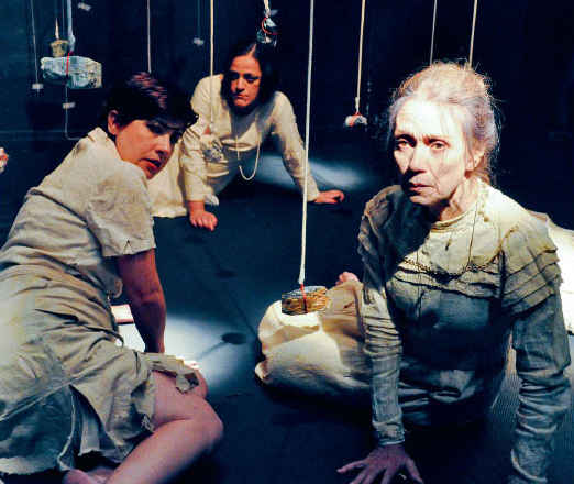 Foto de três atrizes da peça, caracterizadas e sentadas no chão do palco.
