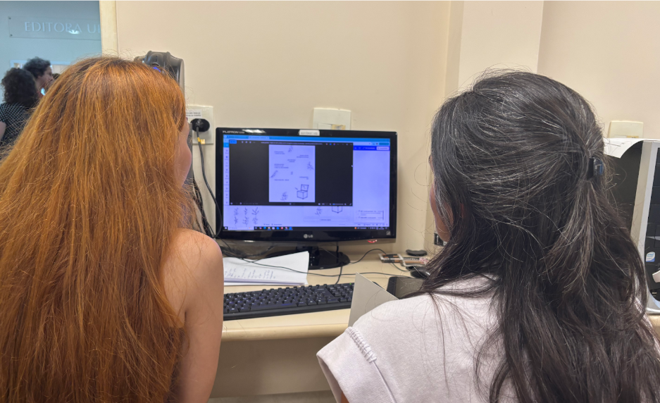Participante da oficina sendo auxiliada pela estagi&aacute;ria na realiza&ccedil;&atilde;o de atividade no Canva 