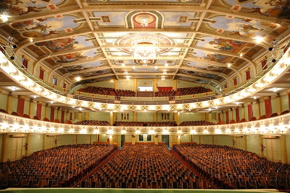 Cine-Theatro Central do ponto de vista do palco, exibindo seus três andares de assentos, pinturas, teto e luzes acesas.