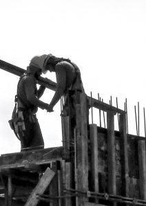 Fotografia em preto e branco de dois profissionais da construção civil trabalhando em uma obra. 