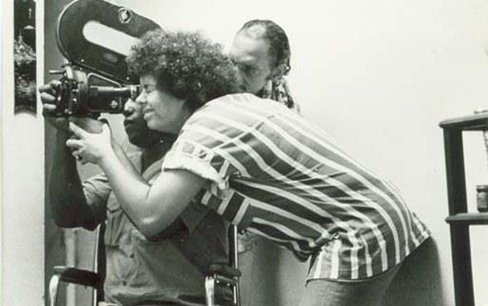 Imagem em preto e branco de Adélia Sampaio manuseando equipamento cinematográfico antigo. 