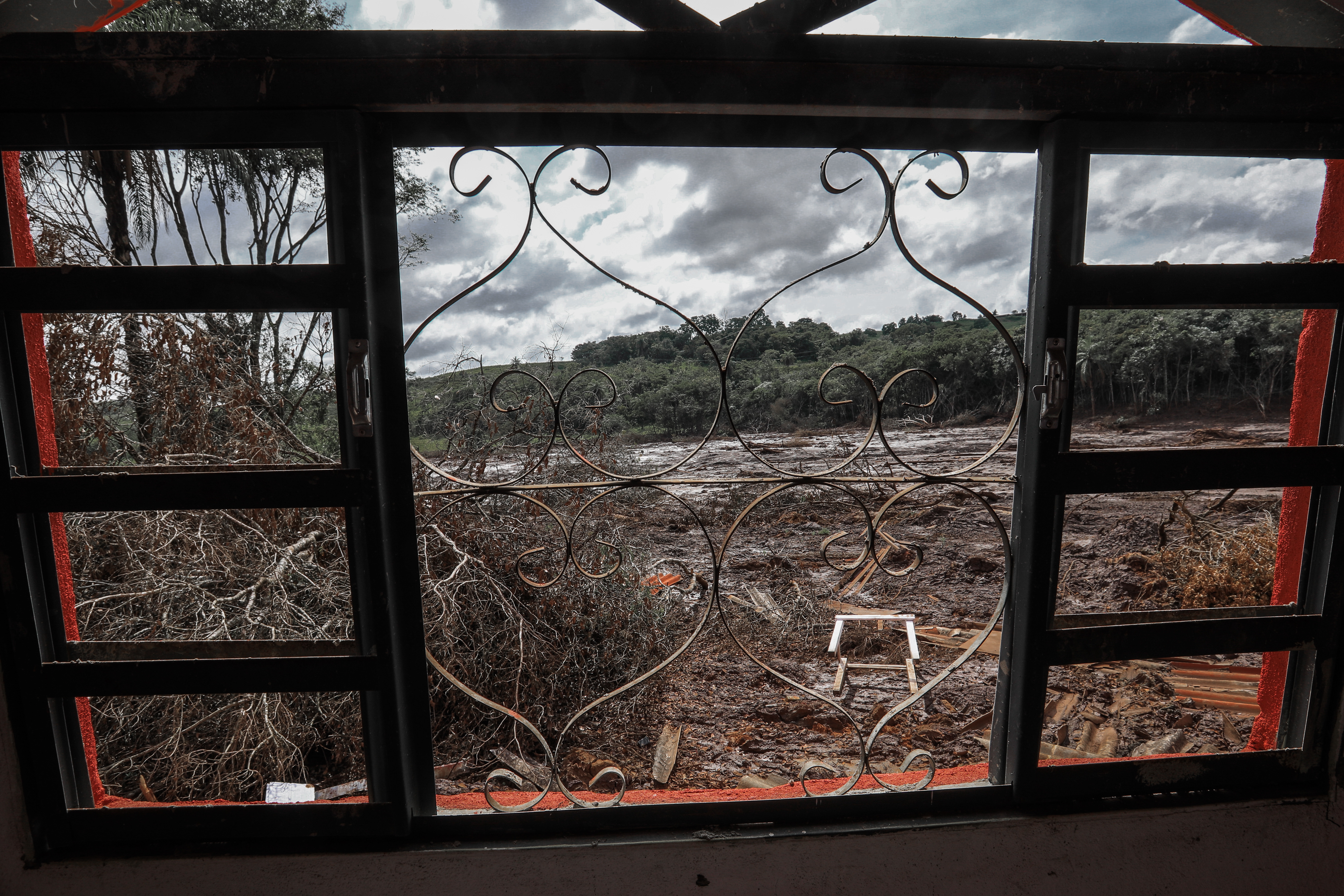 Visão do ambiente devastado pela tragédia em Brumadinho, através de uma janela.